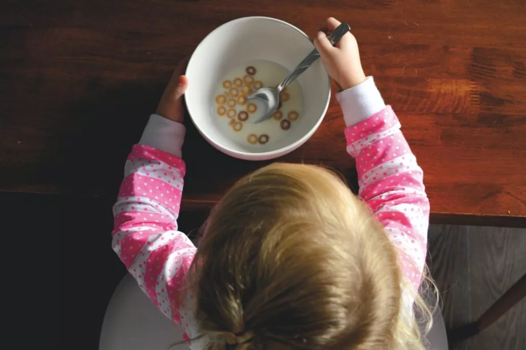 girl eating cereal in white ceramic bowl on table